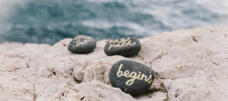 Pebbles on a beach saying "So the path begins"